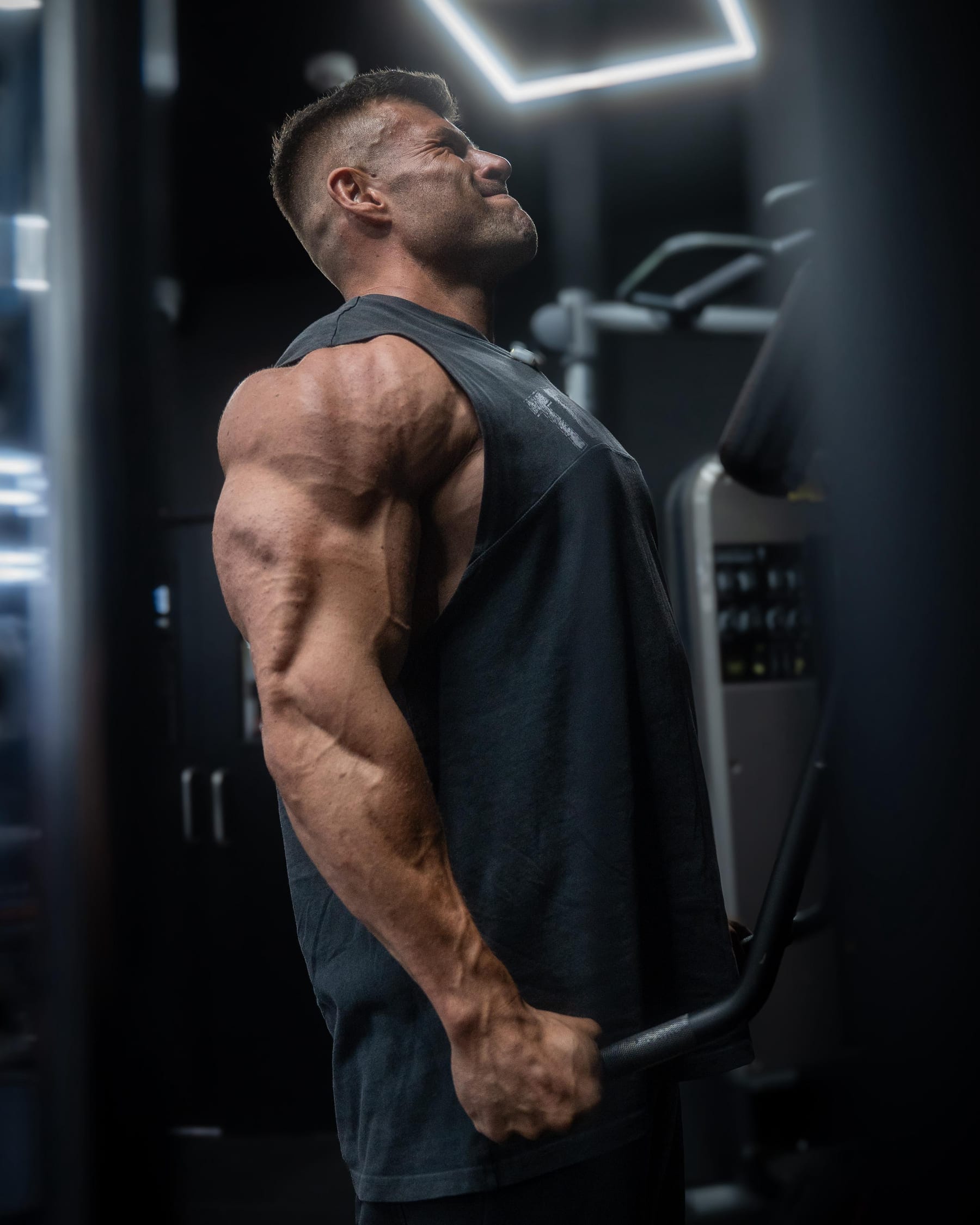 Joey Farrell mid-set on a machine in a dimly lit gym, head back under the effort.