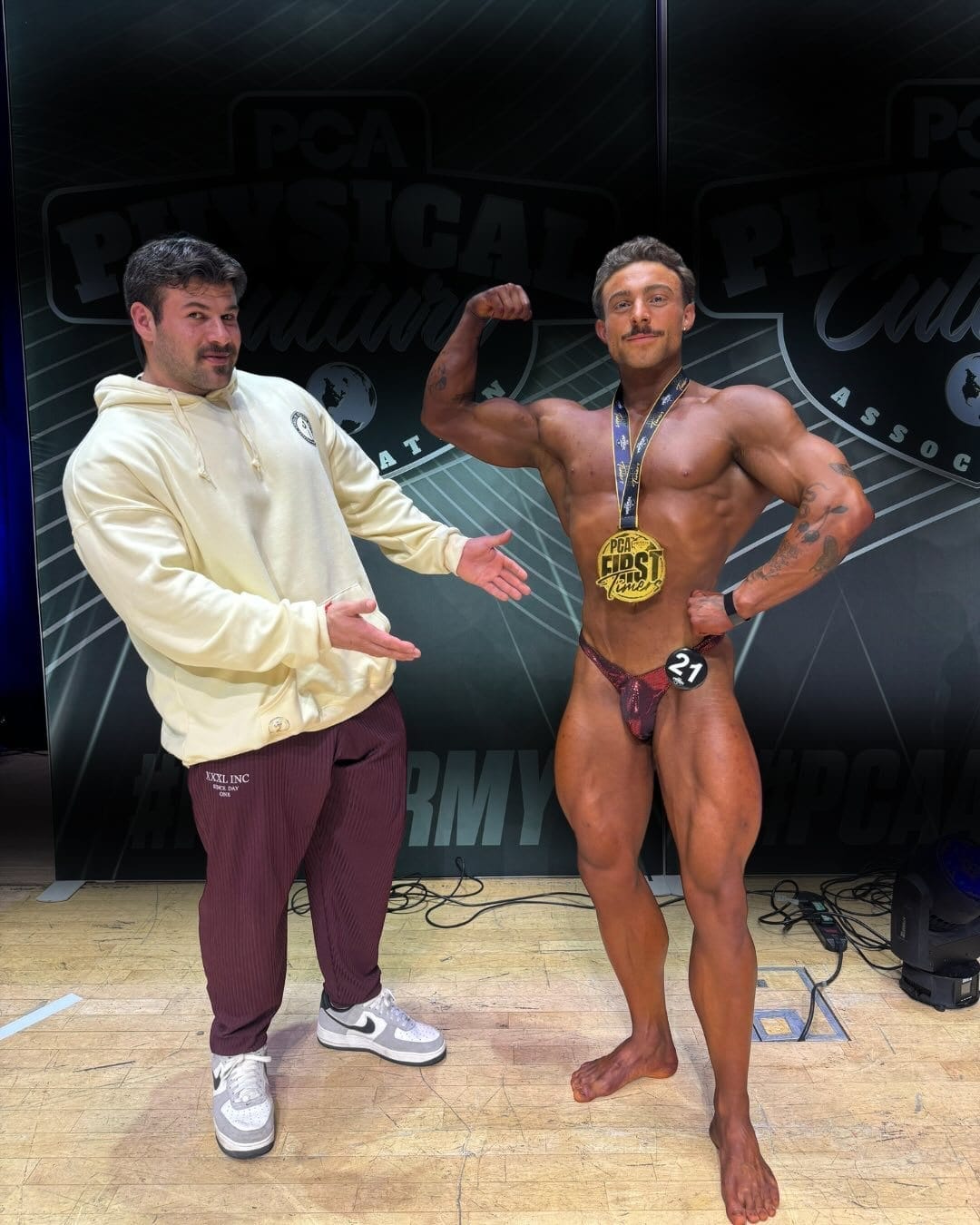 A ProFlow Physiques client on stage at a PCA show, holding a pose with a gold medal around their neck.