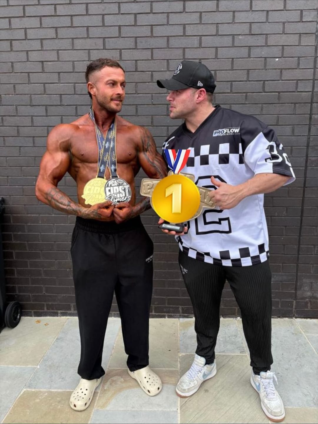 A ProFlow Physiques client outside the venue after competing, wearing the medals they won and holding a first place medal.