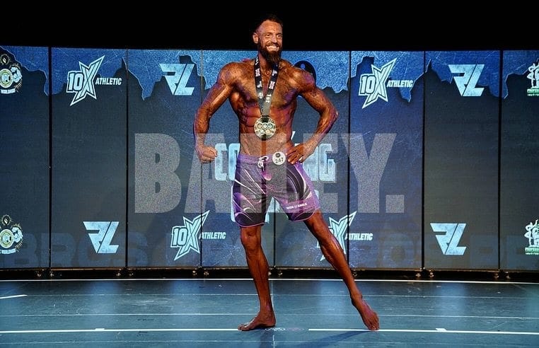 A ProFlow Physiques client on stage under the show lights, posing with their medals around their neck.
